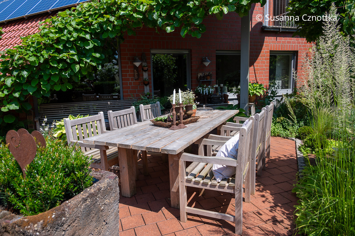 Ein großer schlichter Holztisch ist das Herz des Terrassenzimmers Ein großer schlichter Holztisch mit sechs Stühlen auf einer Terrasse