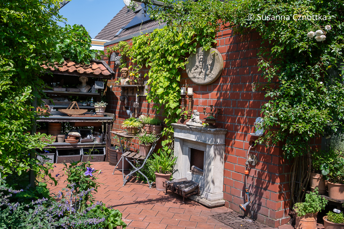 Ein Gartenraum mit einem dekorativen Pflanztisch und einer Kaminattrappe Ein Gartenraum mit einem dekorativen Pflanztisch und einer Kaminattrappe