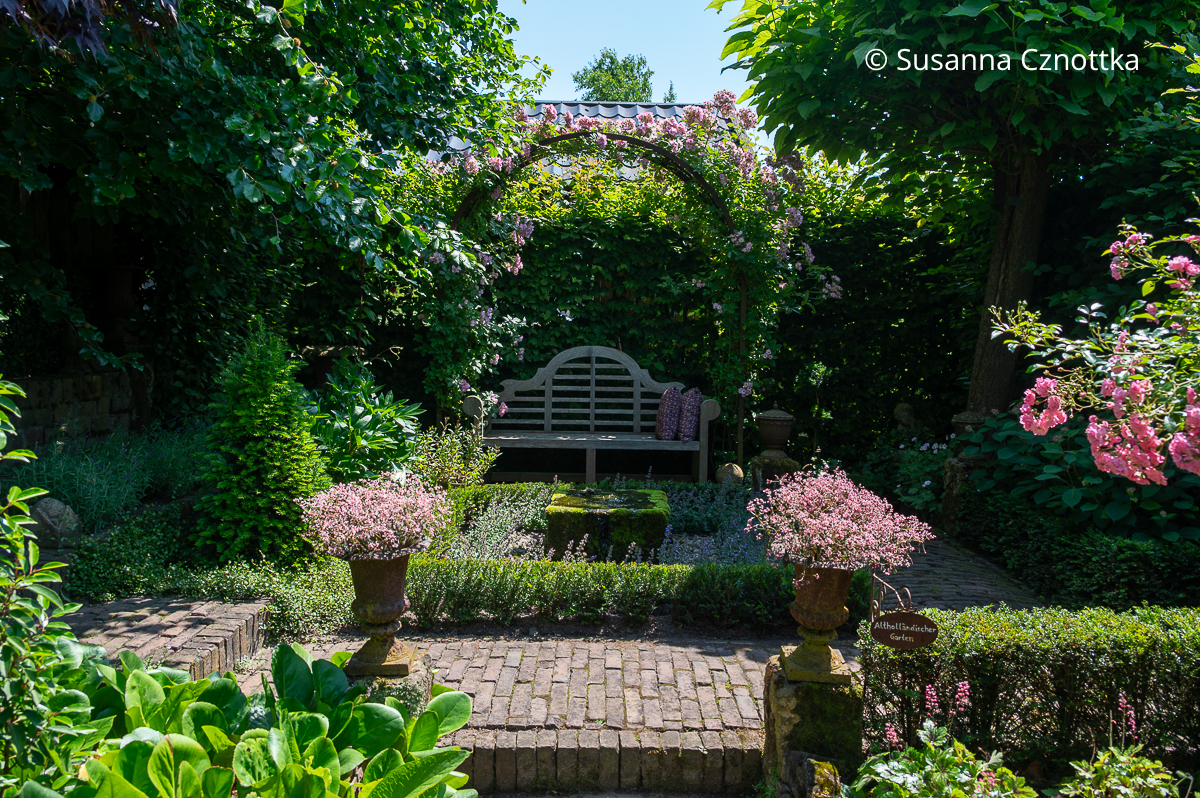 Ein kleiner formaler Garten mit einem Quellstein, rechteckigem mit Eibe eingefassten Beet und einer Lutyens-Bank unter einem Rosenbogen Ein kleiner formaler Garten mit einem Quellstein, rechteckigem mit Eibe eingefassten Beet und einer Lutyens-Bank unter einem Rosenbogen